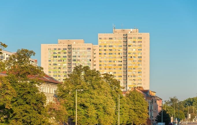 Straßenansicht von zwei hohen Wohnhochhäusern mit gelb-grünen Fensterakzenten hinter grünen Bäumen