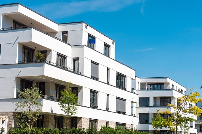 Weißes modernes Mehrfamilienhaus mit Balkonen Klinkersockel und großen Fenstern aus schräger Frontperspektive