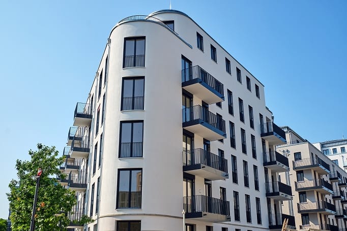 Eckansicht modernes Mehrfamilienhaus mit geschwungener Fassade und schwarzen Balkonen aus bodentiefen Fenstern