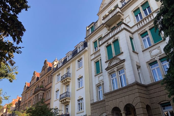 Froschperspektive auf historische Mehrfamilienhäuser mit Balkonen und grünen Fensterläden