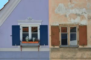 Frontalansicht zweier Wohnhausfassaden mit Fenstern und Klappläden links mit Blumenkasten rechts abblätternder Putz