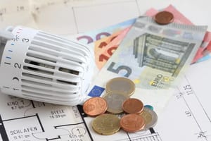 Nahaufnahme eines Heizkörperthermostats auf einem Wohnungsgrundriss mit Euro-Münzen und -Scheinen